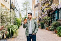 Young smiling man using smart phone on the street in London, England, UK